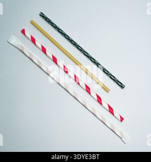Four paper drinking straws with different colors and patterns laid out on a white surface, showcasing eco friendly alternatives to plastic straws. Stock Photo