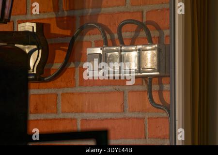 A set of outdoor electrical power outlets with protective covers installed on a red brick wall, connected by black cables and exposed to natural light Stock Photo