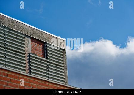 A section of an industrial building featuring brick and concrete materials with a clear blue sky and white clouds in the background. Stock Photo
