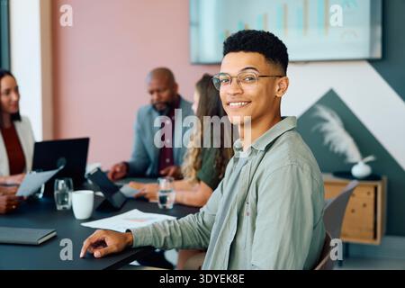 Young businessman sitting confidently and smiling at camera while team works together in boardroom at office Stock Photo