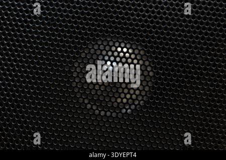 A close-up of a dark speaker grille background texture with a bright central spot. Abstract futuristic technological design. Stock Photo