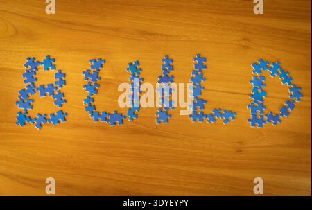 Build concept written with blue puzzle pieces arranged on a wooden table. Conceptual representation of building ideas, business development, teamwork, Stock Photo