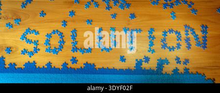 Solution concept written with blue puzzle pieces on a wooden table with scattered pieces around. Creative representation of problem solving, strategy. Stock Photo