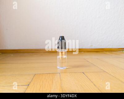A sharp, centered macro shot of a small clear bottle featuring a black dropper cap, resting on a polished wooden surface. The composition emphasizes t Stock Photo