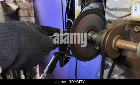 Arms of professional repairman grinding metal details with circular saw at garage. Male hands in protective gloves of mechanic polishing iron using Stock Photo