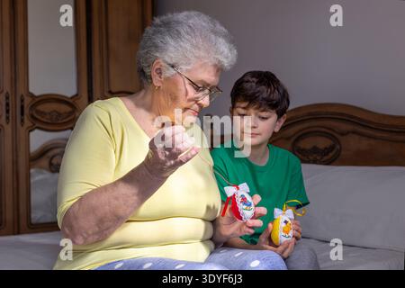 Grandmother teaching her grandson to make decorative Easter eggs during family craft activity at home. Concept of intergenerational connection Stock Photo