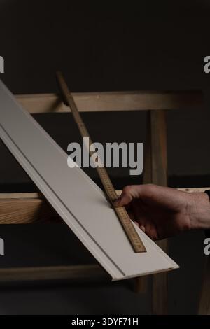 Close up of carpenter holding folding ruler while measuring trim board supported by sawhorses in workshop. Carpentry measuring process for DIY home im Stock Photo