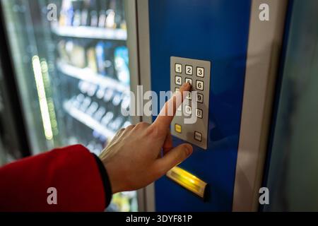 Man customer buying cold drink from automatic vending machine in city, pressing buttons on keypad. Stock Photo