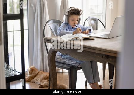 Child writing exercise, listening audio lesson through headphones Stock Photo
