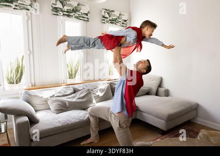 Father lifts son playing superhero, having fun at home Stock Photo