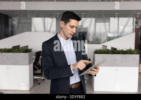 Focused Latin businessman reviewing data on digital tablet in office Stock Photo