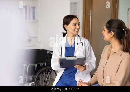 Smiling female doctor holding clipboard, talking to woman patient Stock Photo