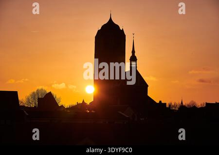 A stunning long shot captures the vibrant orange and golden hues of a sunset or sunrise, with the sun partially obscured by the dark silhouette of a h Stock Photo