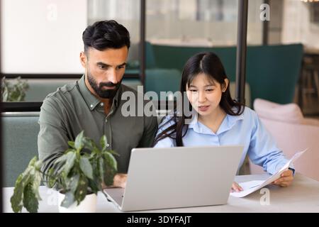 Focused multiethnic team members working together at table in coworking Stock Photo