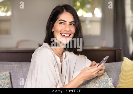 Cheerful young Hispanic woman typing on mobile phone Stock Photo