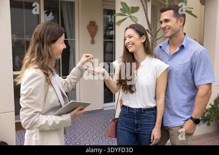 Real estate agent giving house keys to happy couple Stock Photo