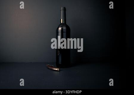 Unlabeled wine bottle with a corkscrew on a dark background and moody studio lighting, ideal for concepts of opening wine, service, tasting ritual and Stock Photo