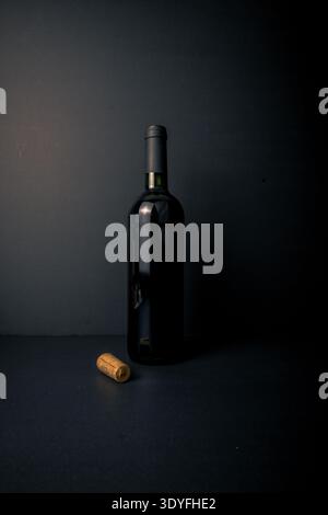 Portrait image of an unlabeled wine bottle with a cork in the foreground on a dark background, a minimalist still life for concepts of uncorking, tast Stock Photo