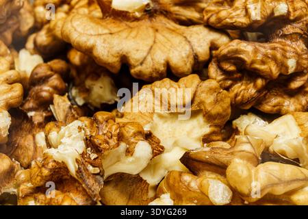 Walnuts are arranged on a surface in a market. The light hits the brown shells. Some halves are visible among the whole nuts. Stock Photo