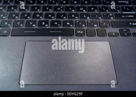 Close view of a laptop keyboard showing keys in different languages and a touchpad on a working surface. Stock Photo