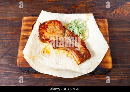 Delicious grilled Pork ribs served on a flatbread with fresh greens on a wooden table Stock Photo
