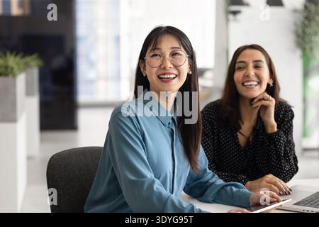 Happy young Asian business professional woman sitting at office table Stock Photo