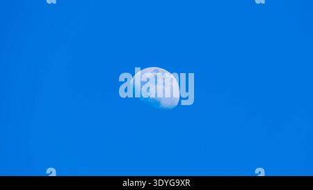 Detailed daytime partial moon against bright blue cloudless sky Stock Photo