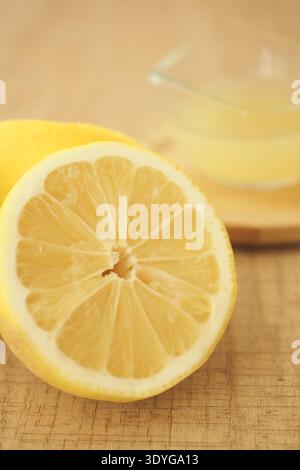 Lemon cut in half on wooden table with lemon juice nearby Stock Photo