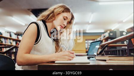 Woman, student or studying with book for education, knowledge or learning in school library. Female person, writing or taking notes with diary or Stock Photo