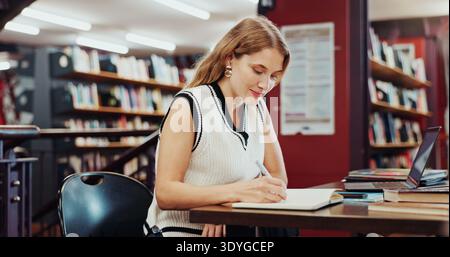 Happy woman, student or writing with book for education, knowledge or learning in school library. Female person, studying or taking notes with diary Stock Photo