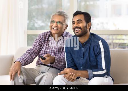 Elderly man and grownup son sitting on couch watching television Stock Photo