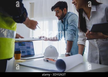 Architects and engineers discussing construction project with blueprint and safety helmet in office Stock Photo