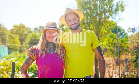 Smiling diverse couple wearing straw hats in urban garden Stock Photo