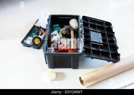 Open black toolbox with power tools and hardware on white floor, construction or DIY project setup Stock Photo