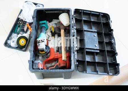 Open black toolbox with power tools and hardware items on white floor in urban workshop Stock Photo