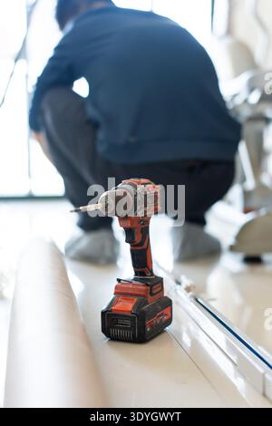 Worker using cordless drill on white surface in modern interior, construction or renovation scene Stock Photo