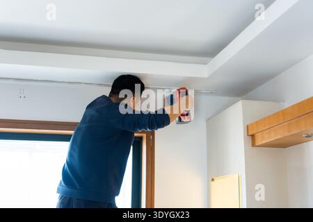 Man using drill to install ceiling fixture in modern home interior, urban apartment renovation in Stock Photo