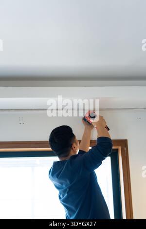 Man installing ceiling fixture using power tool in modern home interior, Shanghai China Stock Photo