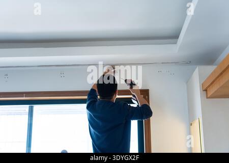 Man installing ceiling light fixture in modern home interior, viewed from behind, urban residential Stock Photo
