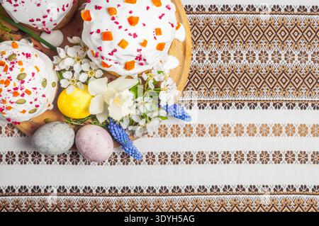 A festive Easter spread featuring decorated cakes, colorful eggs, and blooming flowers arranged on a beautifully embroidered textile Stock Photo