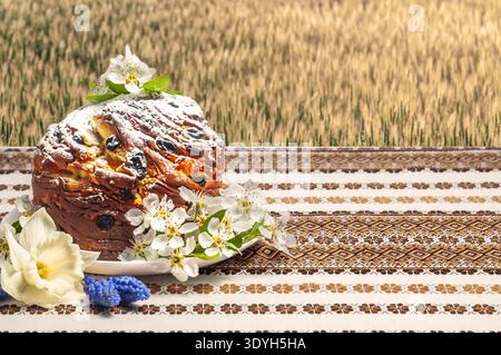 A beautifully decorated Easter bread, known as Paska or Kulich, is presented on a table with a folk-patterned cloth, surrounded by spring blossoms and Stock Photo