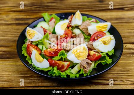 Tasty tuna salad with eggs, lettuce and fresh vegetables on wooden table Stock Photo