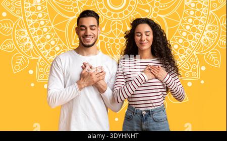 Couple Stands Together With Hands on Hearts in Bright Yellow Backdrop During Joyful Moment Stock Photo
