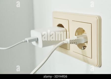 White charger and cable connected to double power outlet on white wall Stock Photo