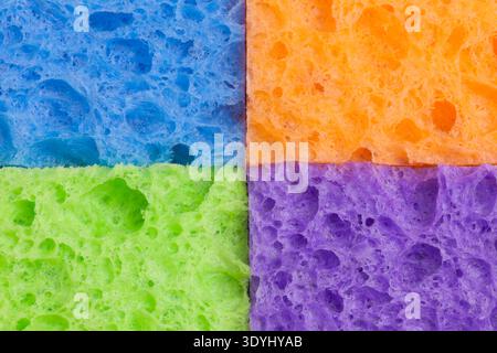 Close-up of four household sponges arranged in a square grid pattern with vivid colors - blue, orange, green, and purple. The porous textures and bold Stock Photo