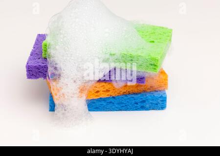 Brightly colored household sponges stacked and covered in foamy soap bubbles against a clean white background. This eye catching image conveys cleanli Stock Photo