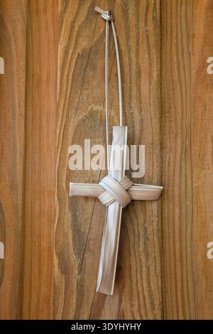 A simple handmade cross crafted from dried palm fronds hangs against a rustic wooden background. This traditional cross, often associated with Palm Su Stock Photo
