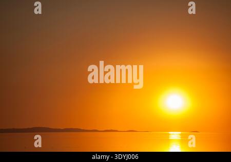 A fiery orange sun sets over the calm surface of the Great Salt Lake, casting golden reflections across the water. Stock Photo