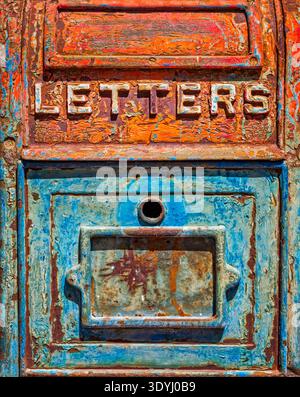 Close up of an antique metal mailbox with peeling turquoise and orange paint and the word LETTERS in relief, showing rust, patina, texture, and bold c Stock Photo