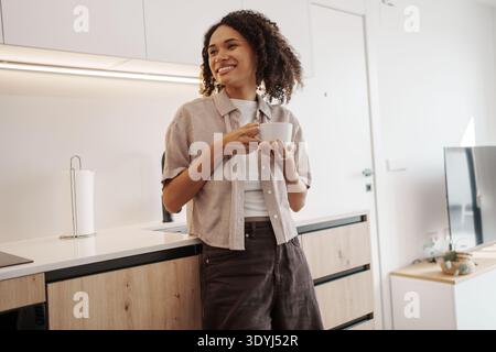 Female Expressing Happiness While Holding Mug In Comfortable Kitchen Environment With Bright Sunlight Stock Photo
